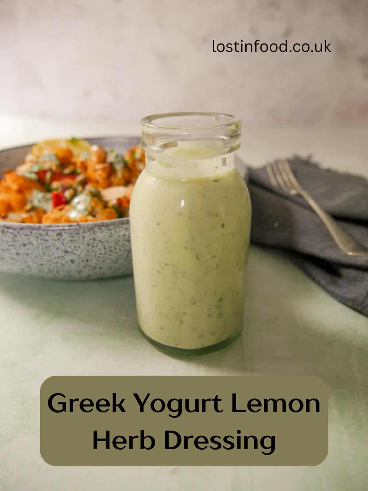 Pinnable image and recipe title with an image of a jar of Greek yogurt lemon herb dressing with a bowl of roasted cauliflower and chickpeas set alongside.