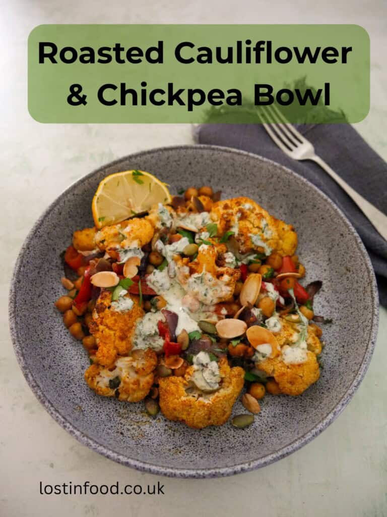 Pinnable image with recipe title and a bowl of roasted cauliflower and chickpeas, drizzled with Greek yogurt lemon herb dressing, and garnished with fresh herbs, and toasted almonds and pumpkin seeds.