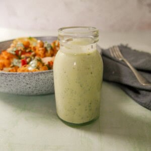 A jar of Greek yogurt lemon herb dressing with a bowl of roasted cauliflower and chickpeas set alongside.