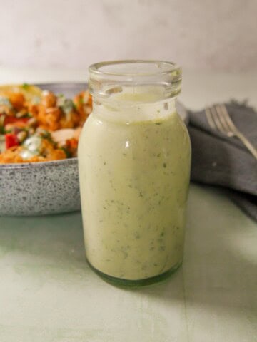 A jar of Greek yogurt lemon herb dressing with a bowl of roasted cauliflower and chickpeas set alongside.