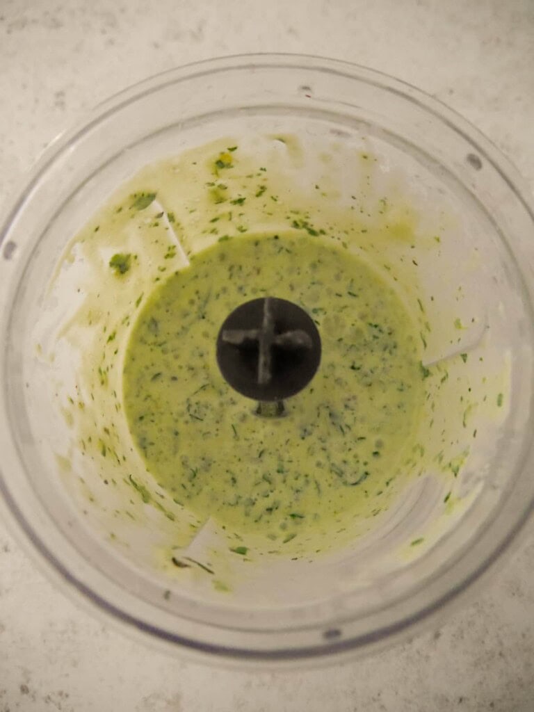 A food processor bowl with blitzed Greek yogurt and lemon herbs dressing.
