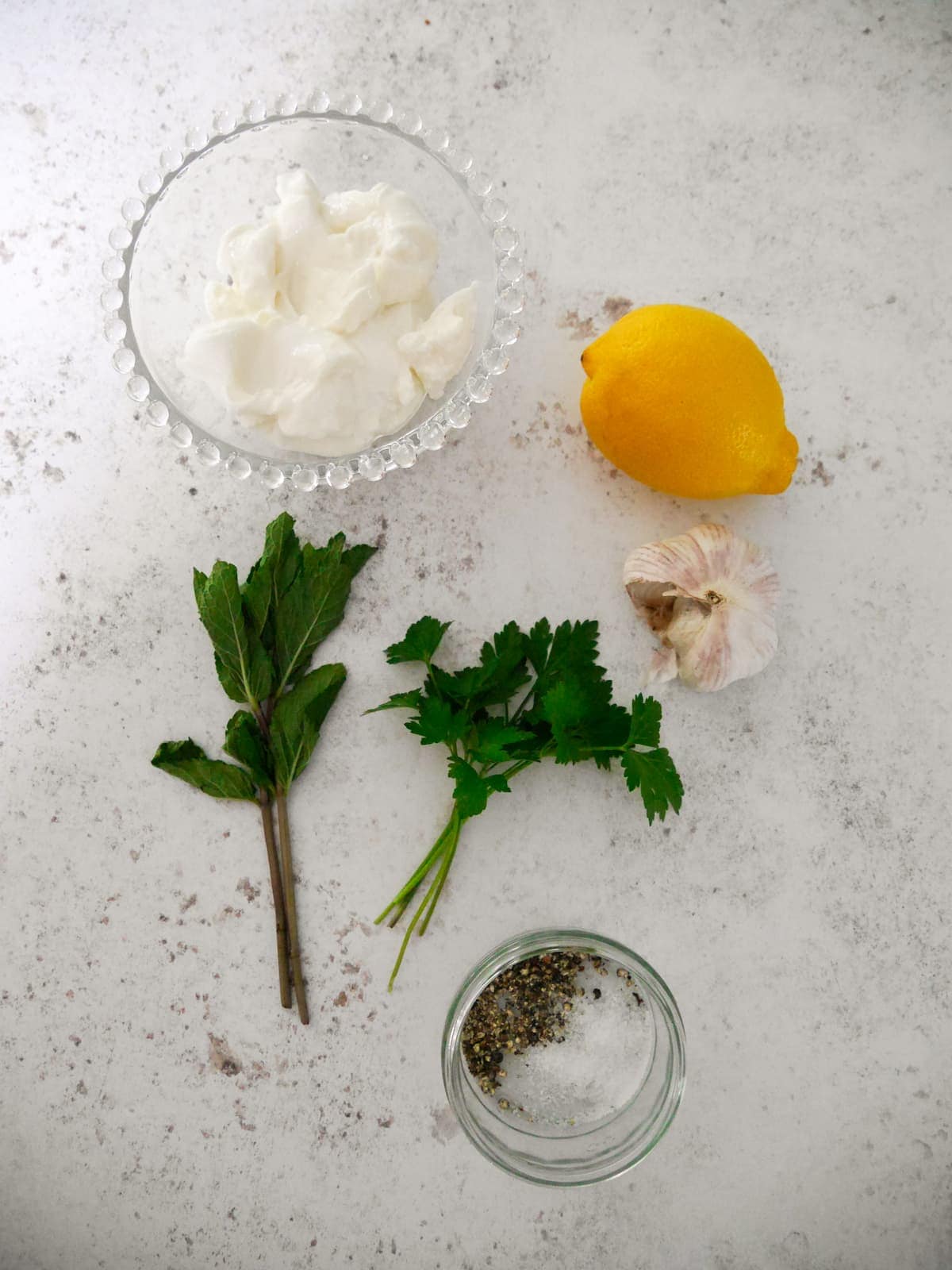 Individual recipe ingredients for making Greek yogurt and lemon herb dressing.