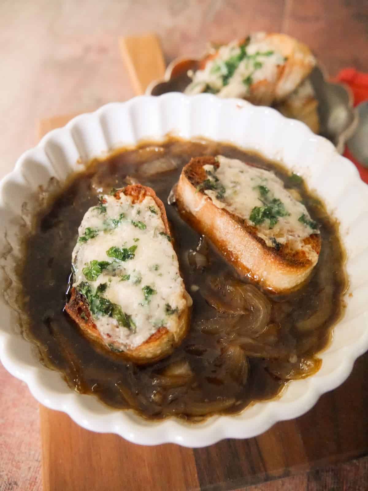 A bowl of French onion soup, topped with slices of toasted baguette topped with melted gruyere cheese.