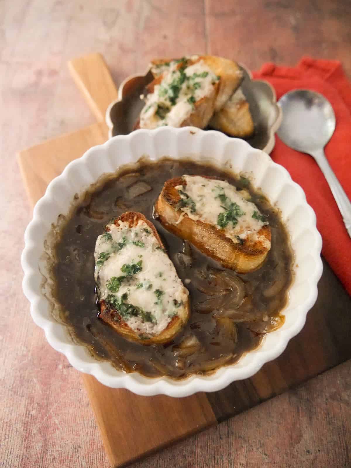 A bowl of French onion soup, topped with slices of toasted baguette topped with melted gruyere cheese.