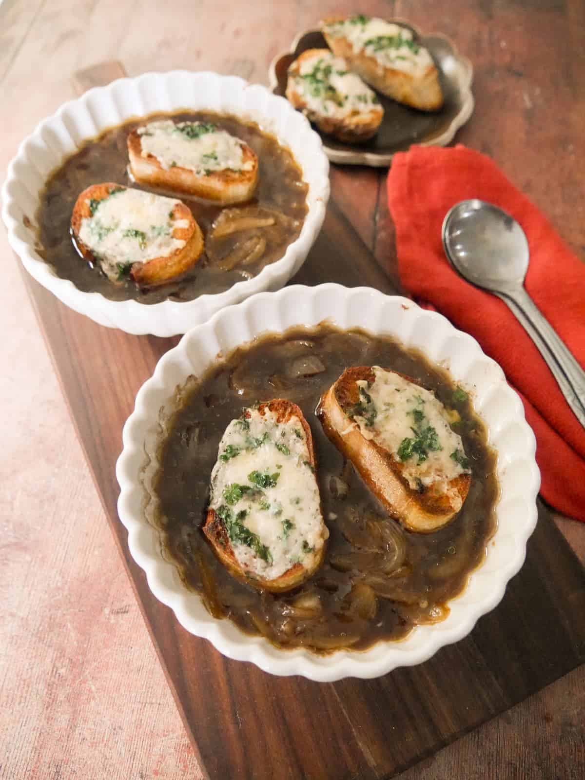 Two bowls of French onion soup, topped with slices of toasted baguette topped with melted gruyere cheese.