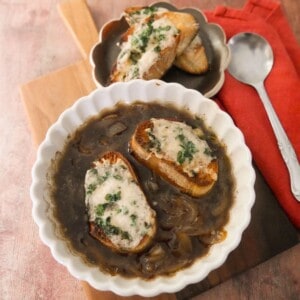 A bowl of French onion soup, topped with 2 slices of toasted baguette topped with melted gruyere cheese.