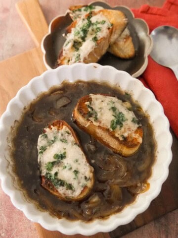 A bowl of French onion soup, topped with 2 slices of toasted baguette topped with melted gruyere cheese.