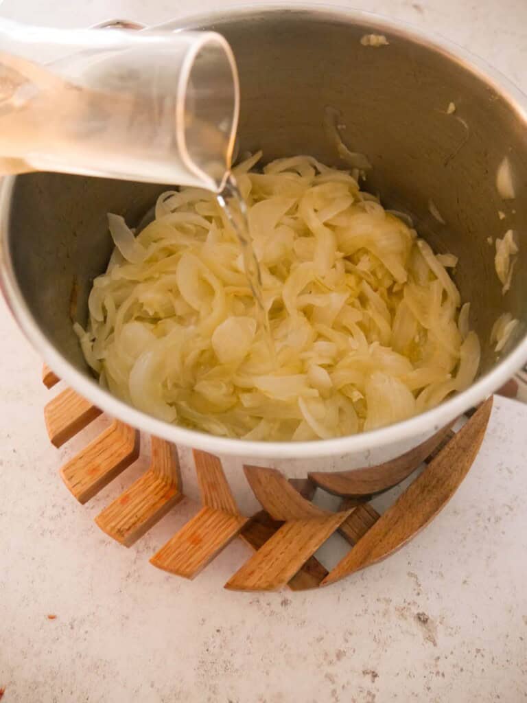 A large saucepan of sauteed onions and garlic with white vermouth being added.