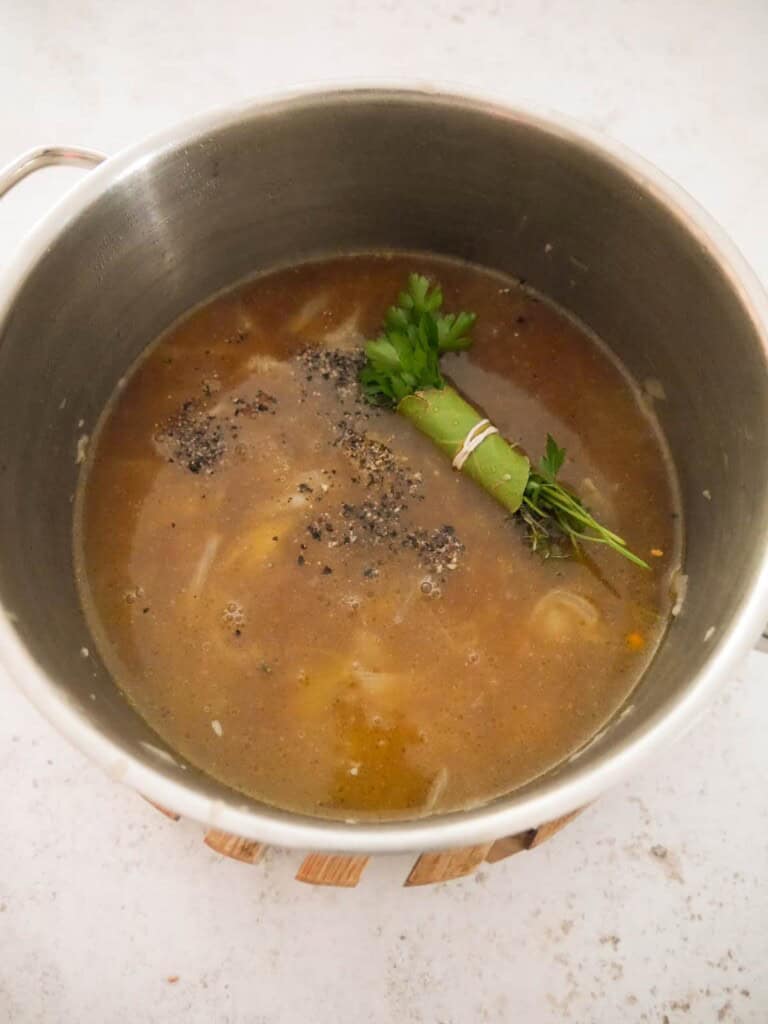 A large saucepan of cooked onions, with added beef stock, bouquet garni and black pepper.