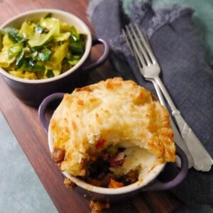 A small dish of masala spiced cottage pie, served with a bowl of mustard spiced cabbage set alongside.