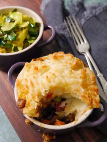 A small dish of masala spiced cottage pie, served with a bowl of mustard spiced cabbage set alongside.