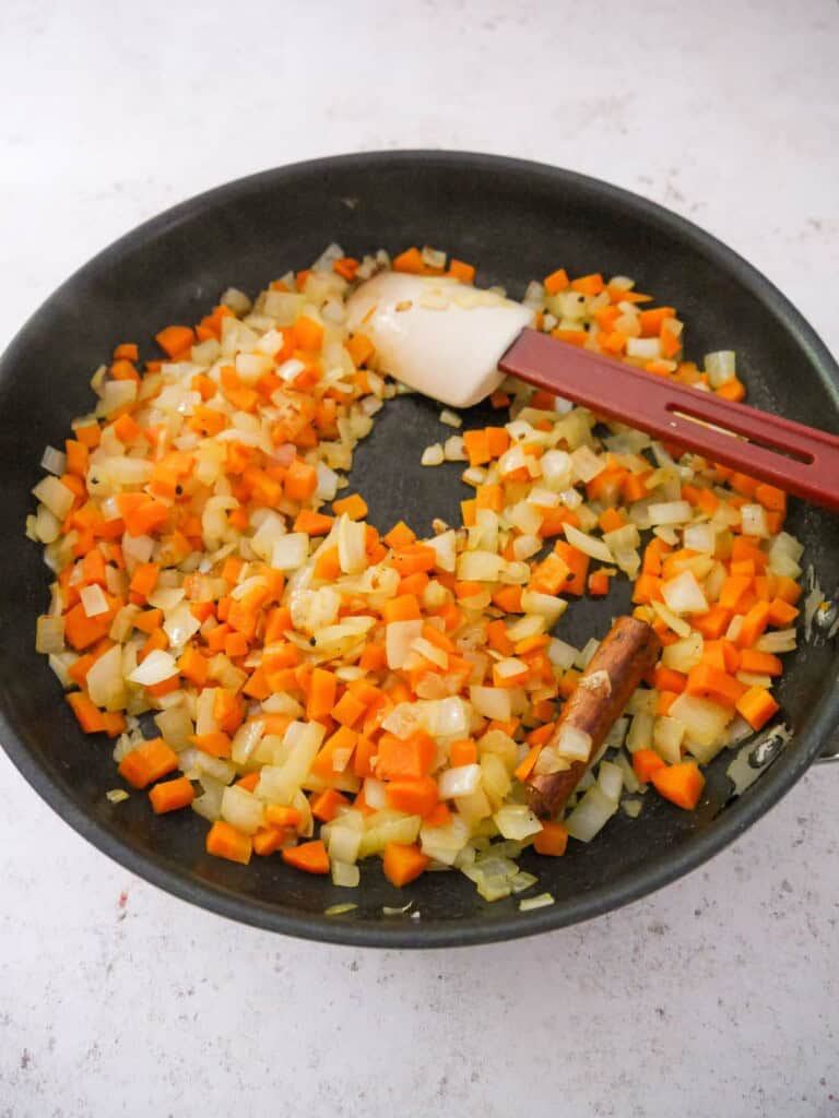 A large frying pan of sauteed onion, carrot, garlic and ginger, with added whole spices.