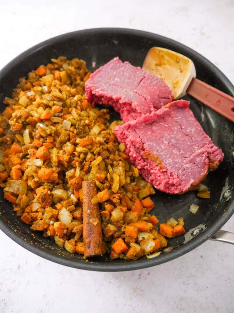 A large frying with spiced, sauteed vegetables with minced beef being added.
