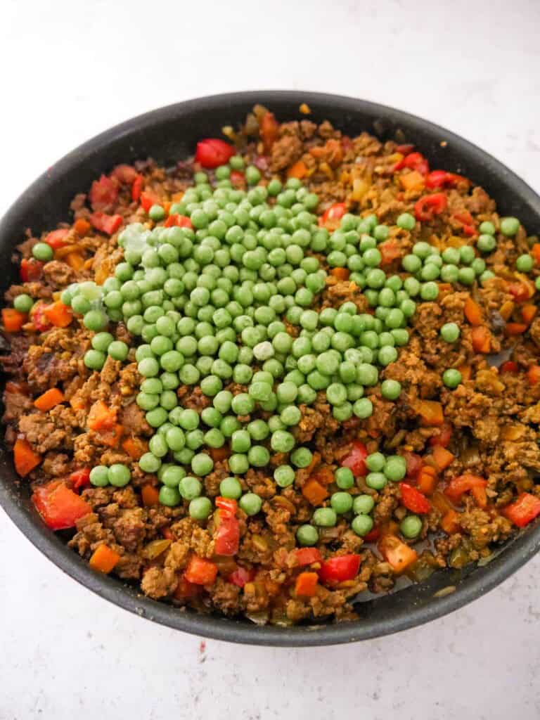 A large frying pan of spiced cooked minced beef and vegetables, with added frozen garden peas.