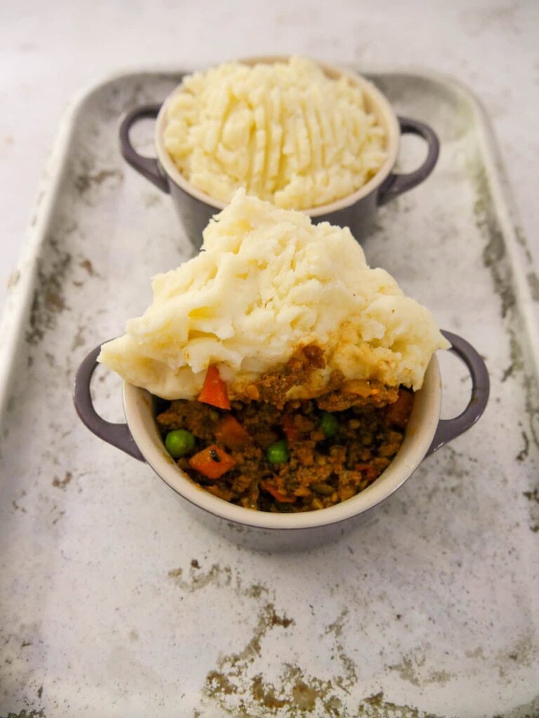 Two dishes of masala spiced cottage pie filling with creamy mashed potatoes being forked over the top.