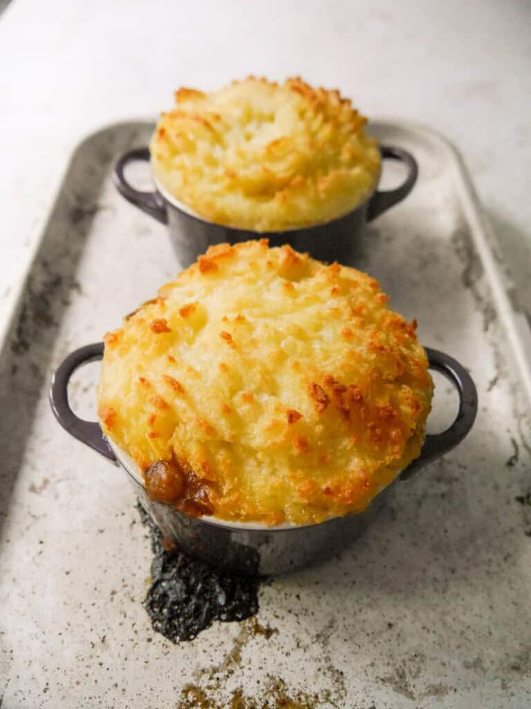 Two individual dishes of baked masala spiced cottage pie, topped with creamy mashed potatoes.